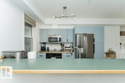 Well-appointed kitchen featuring light blue cabinetry, stainless steel appliances, a modern track lighting fixture, a stainless steel sink with a gooseneck faucet, and a breakfast bar with a speckled green countertop - 