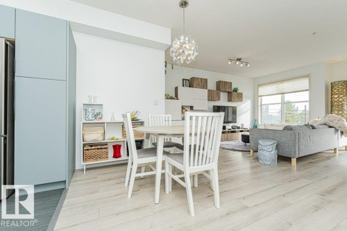 Open-concept living space featuring light wood-finish flooring, a contemporary ceiling light fixture, track lighting, and a large window - #202 9503 101 Av Nw, Edmonton, AB 