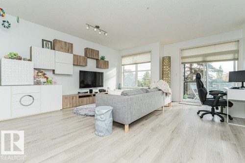 Light wood-finish flooring throughout, track lighting, and a built-in media console with storage - #202 9503 101 Av Nw, Edmonton, AB 