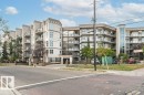Multi-story building featuring balconies with glass railings, an integrated entrance with an arched portico, and a prominent glass and metal elevator shaft - #202 9503 101 Av Nw, Edmonton, AB 