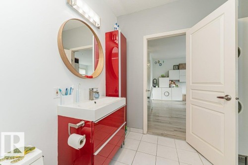 White tiled flooring, vanity with integrated sink, rectangular wood-frame mirror, and a red storage cabinet - #202 9503 101 Av Nw, Edmonton, AB 