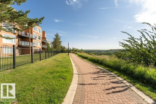 Paved brick pathway with a concrete border, featuring surrounding grassy areas and a distant landscape - #202 9503 101 Av Nw, Edmonton, AB 