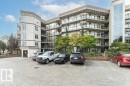 Multi-story building featuring a stucco exterior, multiple private balconies with glass railings, and a large paved parking area - #202 9503 101 Av Nw, Edmonton, AB 