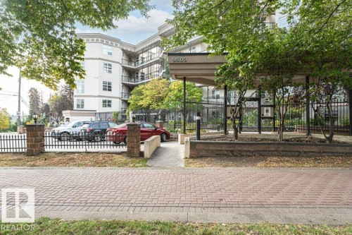 Contemporary building with multiple levels of balconies, a prominent covered entry, and a secure perimeter fence with stone pillars - #202 9503 101 Av Nw, Edmonton, AB 