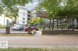 Contemporary building with multiple levels of balconies, a prominent covered entry, and a secure perimeter fence with stone pillars - 