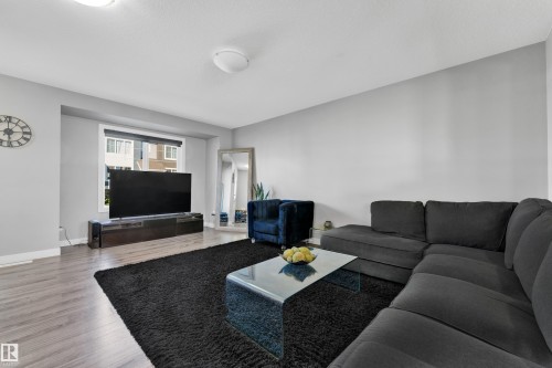 Spacious living area with wood-finish flooring, light gray walls, and a large window providing natural illumination - #22 4205 30 St Nw, Edmonton, AB 
