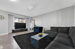 Spacious living area with wood-finish flooring, light gray walls, and a large window providing natural illumination - 