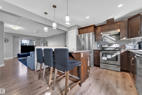 Kitchen island with pendant lighting, wood-finish flooring, stainless steel appliances, dark wood-finish cabinetry, and a tile backsplash - #22 4205 30 St Nw, Edmonton, AB 