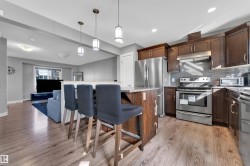 Kitchen island with pendant lighting, wood-finish flooring, stainless steel appliances, dark wood-finish cabinetry, and a tile backsplash - 