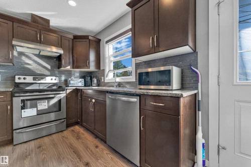 Stainless steel appliances, wood-finish flooring, dark wood cabinetry, light-toned countertops, and a tiled backsplash - #22 4205 30 St Nw, Edmonton, AB 