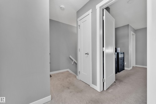 Carpeted hallway with white trim, solid core doors, and a staircase with a handrail - #22 4205 30 St Nw, Edmonton, AB 