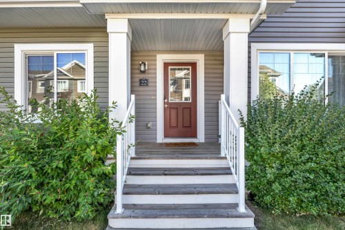 Covered entry with two substantial pillars, wood-finish steps with white railings, a red paneled door with window, and horizontal siding - #22 4205 30 St Nw, Edmonton, AB 