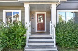 Covered entry with two substantial pillars, wood-finish steps with white railings, a red paneled door with window, and horizontal siding - 