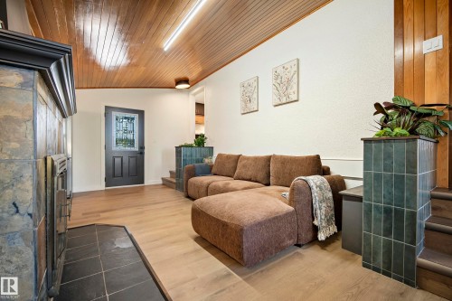 Natural wood plank ceiling, slate tile fireplace surround, wood-finish flooring, decorative entry door with leaded glass, and tiled half-wall - 10316 42 Street Nw, Edmonton, AB 