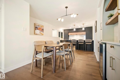 Wood-finish flooring throughout, modern light fixture, built-in shelving, integrated beverage cooler, and kitchen with dark cabinetry - 10316 42 Street Nw, Edmonton, AB 