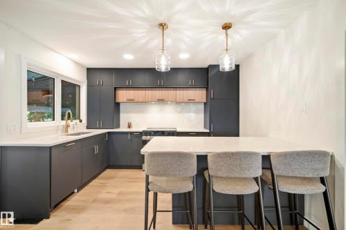 Modern kitchen featuring dark cabinetry, light wood-finish accents, and a white countertop island - 10316 42 Street Nw, Edmonton, AB 
