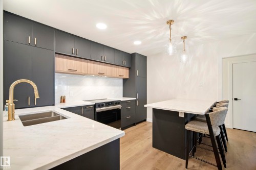 Modern kitchen featuring dark cabinetry with gold-tone hardware, wood-finish accent cabinets, and white countertops - 10316 42 Street Nw, Edmonton, AB 