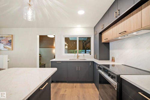 Modern kitchen featuring two-tone cabinetry, light-toned countertops, a built-in range, wood-finish flooring, and a single basin sink with a gold-tone faucet - 10316 42 Street Nw, Edmonton, AB 