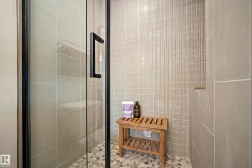 Frameless glass shower enclosure with matte black hardware, pebble-tiled shower floor, and vertical subway tile accent wall - 10316 42 Street Nw, Edmonton, AB 