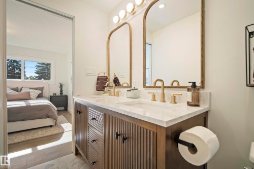 Double vanity with a white countertop and dual undermount sinks, featuring gold-toned fixtures and arched mirrors - 10316 42 Street Nw, Edmonton, AB 