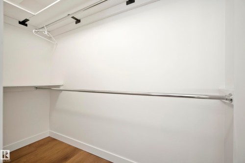 Built-in closet with wood-finish flooring, white walls, and chrome hanging rods - 10316 42 Street Nw, Edmonton, AB 