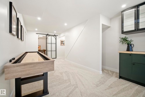Recessed lighting, light-toned carpeting, built-in cabinetry with a wood-finish countertop, dark-toned upper cabinetry with fluted glass, and a black framed sliding barn door - 10316 42 Street Nw, Edmonton, AB 