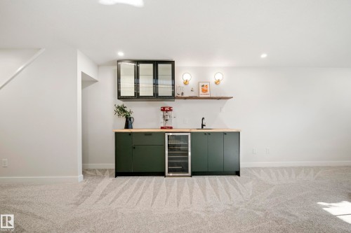Built-in wet bar with wood-finish countertop, under-counter beverage refrigerator, dark green cabinetry, and a floating wood shelf - 10316 42 Street Nw, Edmonton, AB 