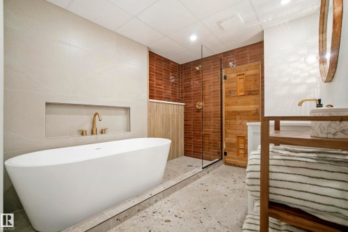 Freestanding bathtub with brass-finish faucet, glass-enclosed shower, wood-paneled sauna door, and terrazzo-style flooring - 10316 42 Street Nw, Edmonton, AB 