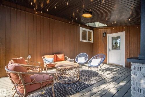 Covered deck with a wood-finish ceiling, vertical wood-panel siding, and a white entry door with decorative glass - 10316 42 Street Nw, Edmonton, AB 