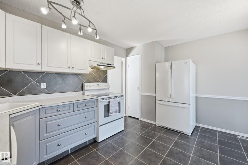 Kitchen featuring white upper cabinetry, grey lower cabinetry, a dark tiled backsplash, white appliances, and a tiled floor - 74 Aspen Crescent, St. Albert, AB 
