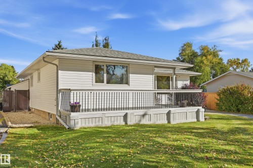 White siding exterior with a large front deck, dark metal deck railing, and a manicured lawn - 74 Aspen Crescent, St. Albert, AB 