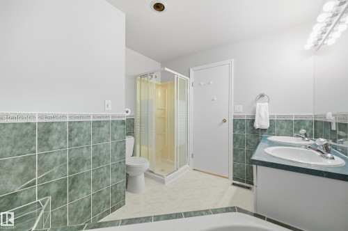 Dual basin vanity with chrome fixtures, tiled shower enclosure, and green wall tiling - 74 Aspen Crescent, St. Albert, AB 