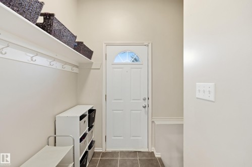 Entry area featuring a solid panel door with an arched window, tile flooring, and wall-mounted coat hooks - 74 Aspen Crescent, St. Albert, AB 