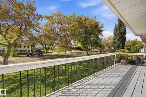 Expansive outdoor deck with composite decking and metal railings, overlooking a tree-lined street and green landscaping - 74 Aspen Crescent, St. Albert, AB 