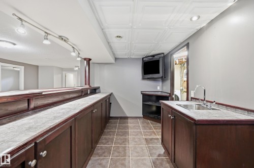 Built-in bar with wood-finish cabinetry, track lighting, a dedicated sink, and tiled flooring - 74 Aspen Crescent, St. Albert, AB 