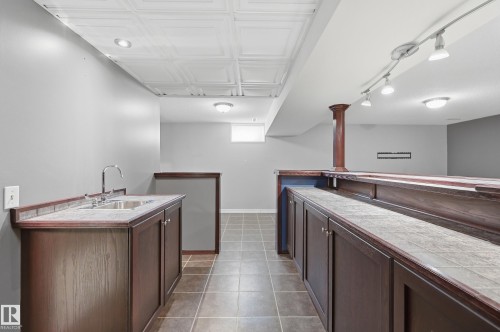 Built-in wet bar with wood-finish cabinetry, tiled countertop, and stainless steel sink - 74 Aspen Crescent, St. Albert, AB 