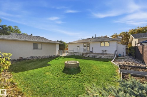 Expansive backyard featuring a central fire pit, manicured lawn, and a multi-level deck with white railings - 74 Aspen Crescent, St. Albert, AB 