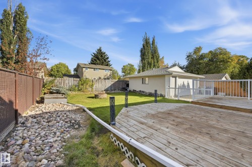 Expansive backyard featuring a large wooden deck, detached structure, and a rock-filled drainage area with a chain-link fence - 74 Aspen Crescent, St. Albert, AB 