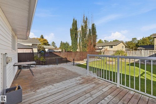 Expansive wood-finish deck with a white metal railing overlooking a manicured lawn - 74 Aspen Crescent, St. Albert, AB 