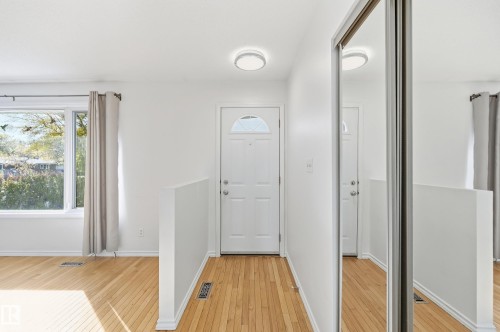 White entry door with decorative glass insert, wood-finish flooring, recessed lighting, and mirrored closet doors - 74 Aspen Crescent, St. Albert, AB 