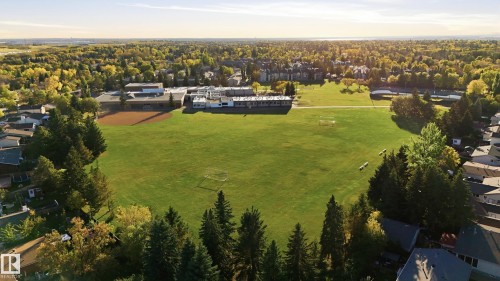 Expansive green space bordered by mature trees and residential structures, with a distant city skyline - 74 Aspen Crescent, St. Albert, AB 