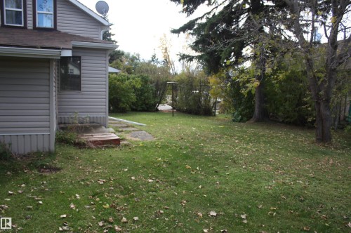 Green lawn with mature trees and established perimeter shrubs - 5012 49 Ave, Radway, AB 