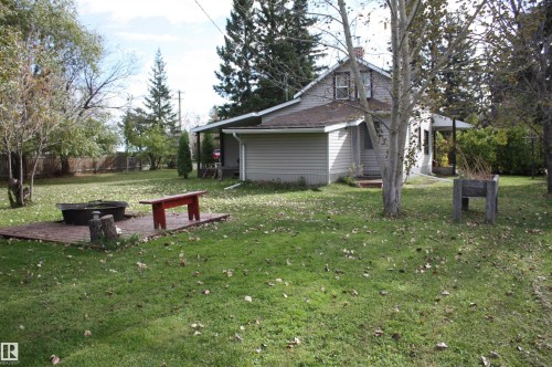 Expansive backyard featuring a brick patio with a built-in fire pit, mature deciduous and evergreen trees, and a privacy fence - 5012 49 Ave, Radway, AB 