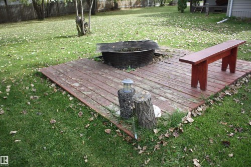 Expansive grassy yard featuring a wood-plank patio, a fire pit, and a wooden bench - 5012 49 Ave, Radway, AB 