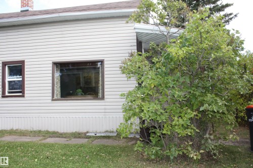 Light-colored horizontal siding exterior with dark-trimmed windows, a prominent brick chimney, and a white gutter system - 5012 49 Ave, Radway, AB 