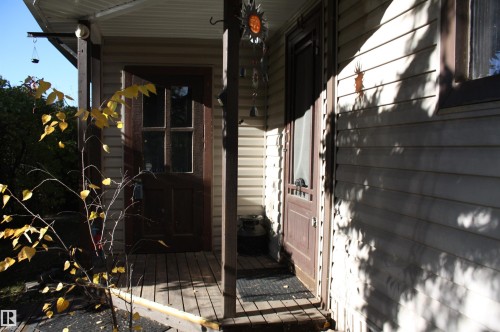 Covered porch featuring horizontal siding, wooden decking, and dual exterior entry doors - 5012 49 Ave, Radway, AB 