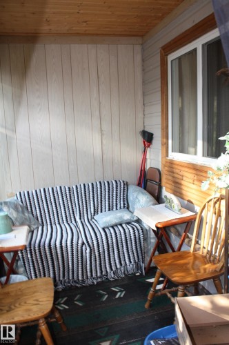 Covered outdoor patio featuring vertical wood-finish paneling, horizontal wood trim, and a window with a wood-finished frame - 5012 49 Ave, Radway, AB 
