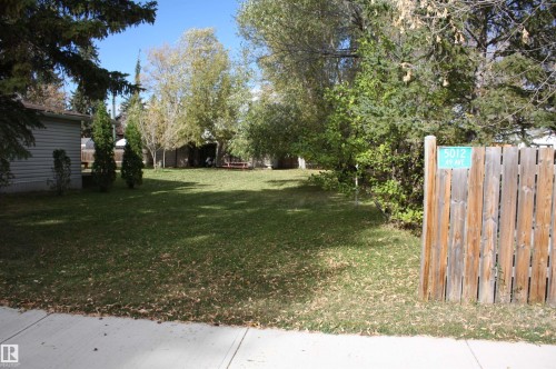 Expansive lot featuring a green lawn, mature trees, and a wood fence - 5012 49 Ave, Radway, AB 