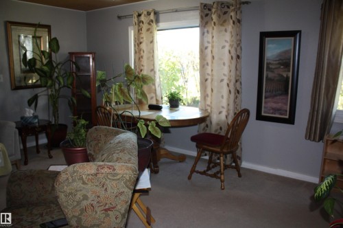 Neutral-toned interior space featuring a large window with natural light and wall-to-wall carpeting - 5012 49 Ave, Radway, AB 
