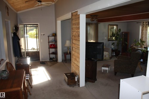 Vaulted ceiling featuring natural wood-finish planking, complemented by an exposed structural column with vertical wood siding and a beamed ceiling accent - 5012 49 Ave, Radway, AB 